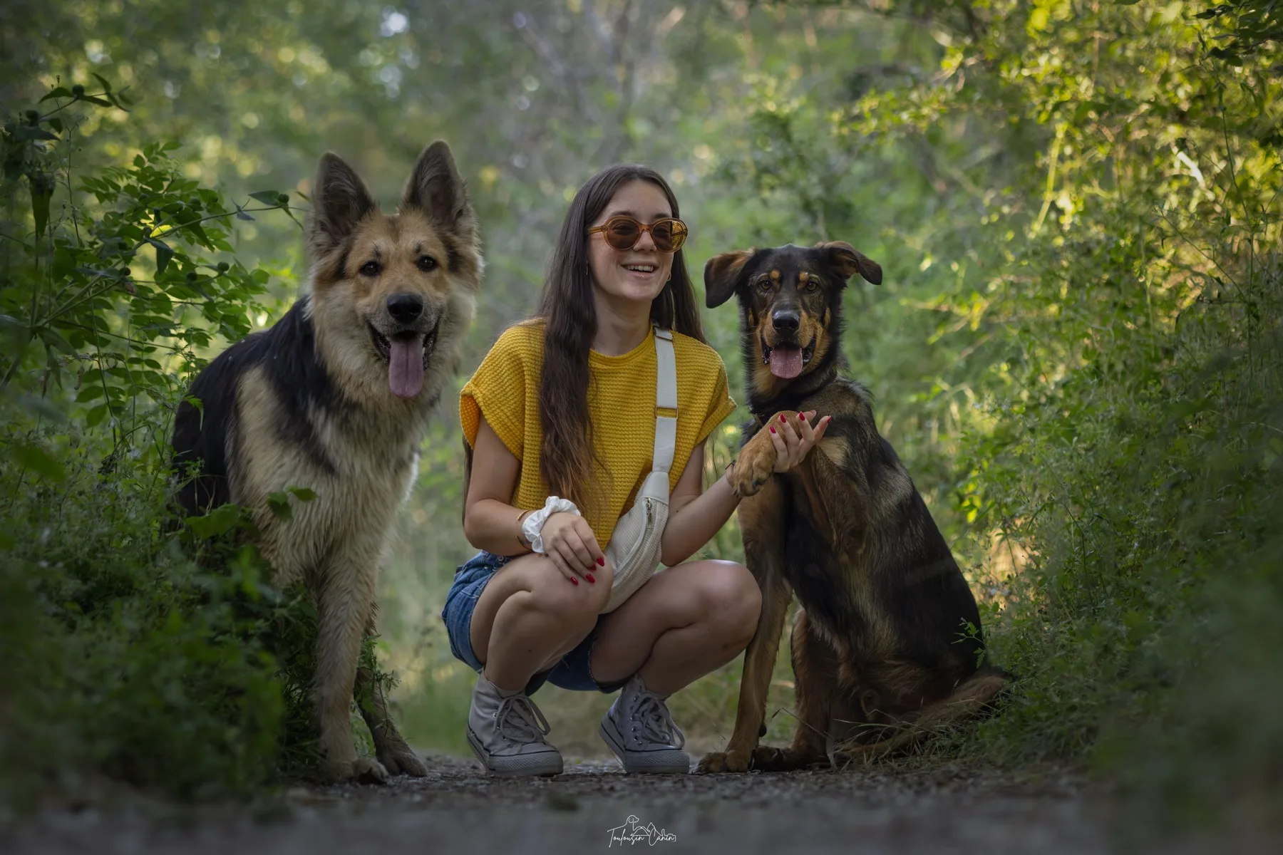Manon accroupie entre ses deux chiens sur un chemin